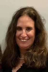 Woman wearing pearls and smiling at camera.