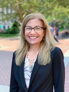 Woman in suit, smiling from campus.