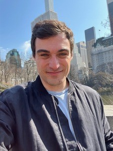 Man smiling against trees and NY skyline.