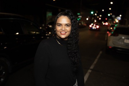 Woman smiling, with cars and city in background.