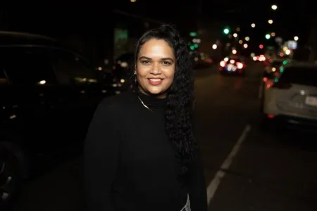 Woman smiling, with cars and city in background.